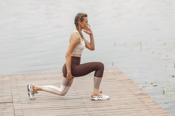 A woman performs lunges on a lakeside wooden deck, showcasing a fit lifestyle outdoors.